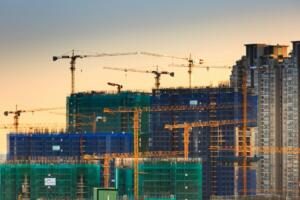 Prédios em construção com telas de proteção e várias gruas em obra de grande porte ao entardecer