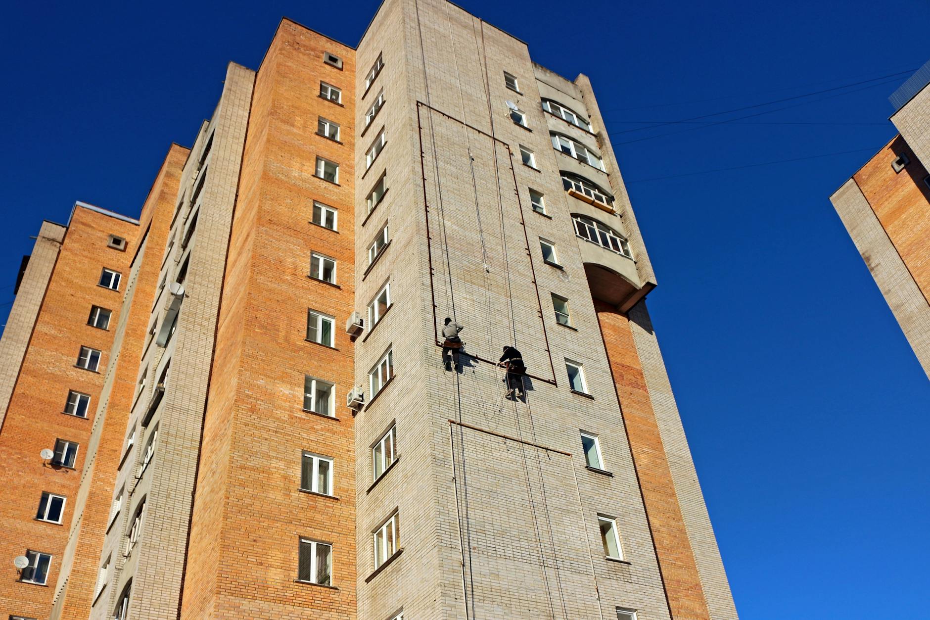 Trabalhadores em alpinismo industrial fazem manutenção na fachada de tijolos de um edifício residencial alto