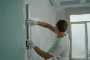 Profissional com luvas aplica massa em parede com desempenadeira durante reforma de apartamento