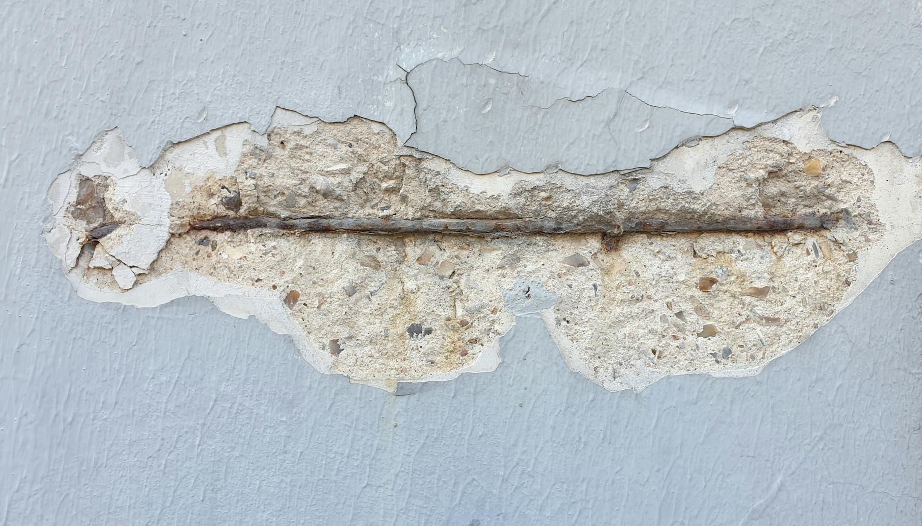Concreto desplacado com armadura de aço corroída exposta em parede, patologia comum na construção