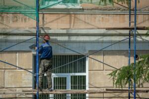 Operário em andaime com tela de proteção trabalha na reforma de fachada de prédio residencial