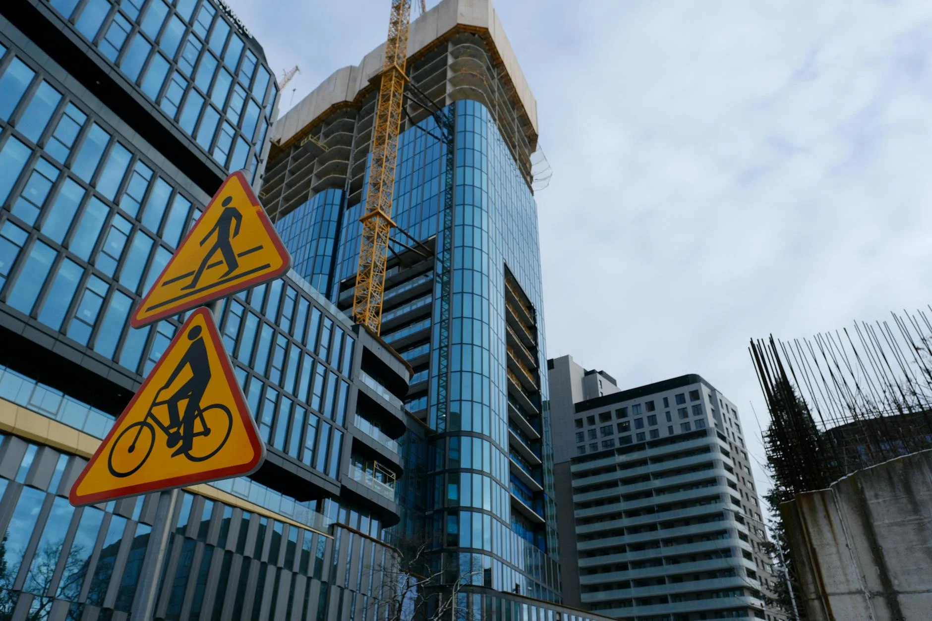 Prédios com fachada de vidro e grua de obra ao lado de placas de pedestres e ciclistas